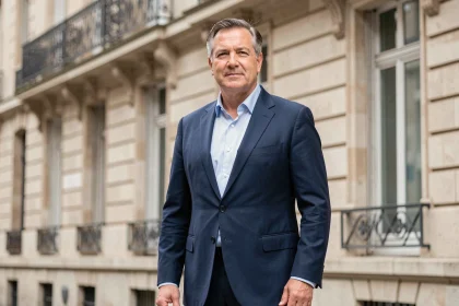 Portrait d'un homme d'âge mûr en costume bleu marine devant un immeuble haussmannien parisien, illustrant un article sur Jean Jacques Trogneux et sa ressemblance avec Emmanuel Macron